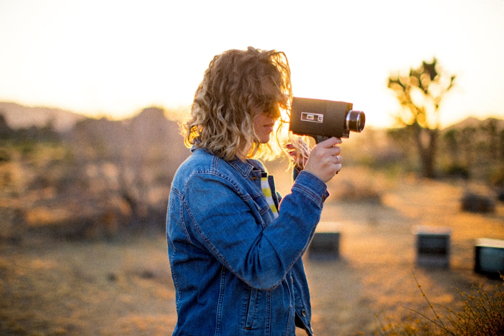 woman wearing blue denim jacket holding classic camcorder
