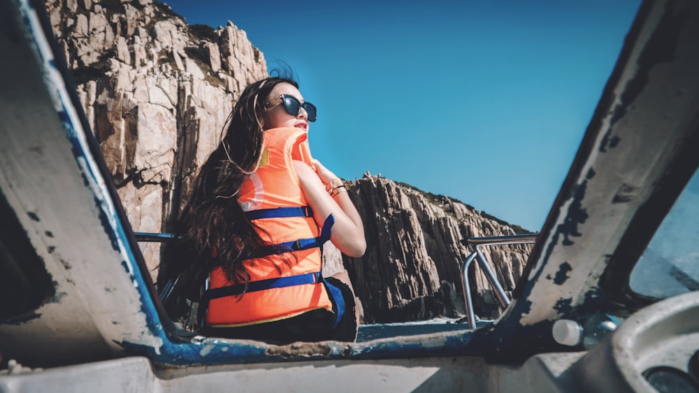 woman with life vest sitting on boat facing brown mountain