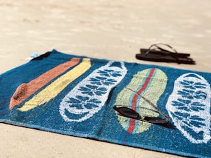 black sunglasses on blue towel beside pair of black flip-flops