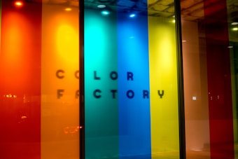 A vibrant display featuring vertical panels of translucent colors, including red, orange, yellow, blue, and green. The text 'COLOR FACTORY' is subtly visible behind the panels, casting a shadow effect.