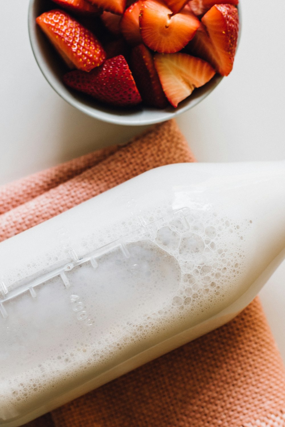 closeup photo of milk bottle beside slice strawberries in white bowl
