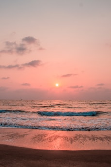 A serene coastal view of a Sicilian beach at sunset, with gentle waves lapping at the shore.