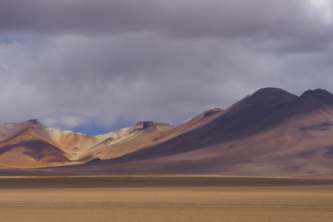 a group of mountains in the distance under a cloudy sky, A scene from a small desert valley on the way to the Salar de U