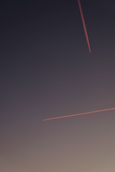 Two contrails from airplanes are visible against a dusky sky, one descending diagonally from the top right and the other moving horizontally toward the center.