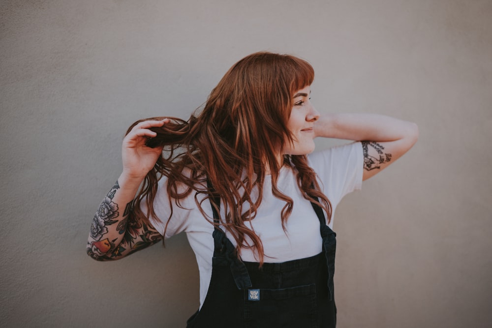 woman holding her hair standing against gray wall