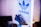 A stylish sneaker is placed beside a panel displaying the Adidas logo, featuring bold blue and white colors. The shoe is predominantly dark with neon green accents and has a modern, sporty design.