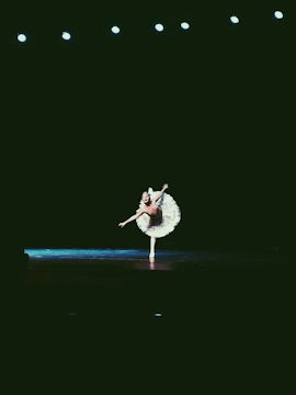 A graceful ballet dancer performing under warm stage lights in an elegant theater.