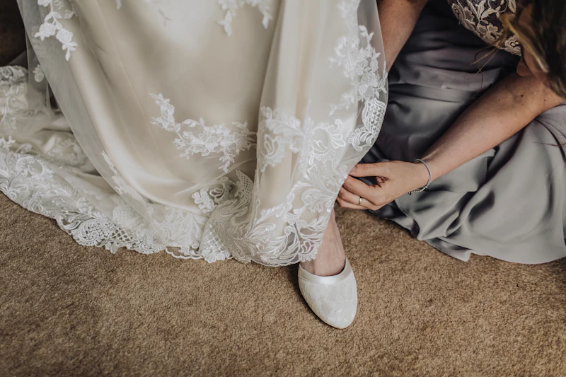 Bridesmaid helping bride with her shoes