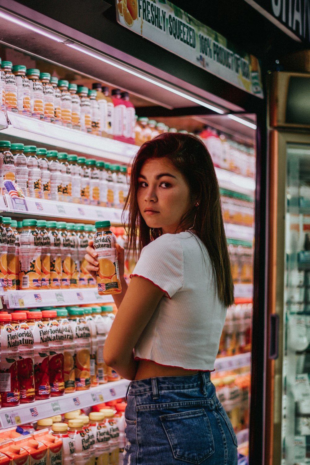 Mujer sosteniendo una botella etiquetada frente a un refrigerador comercial
