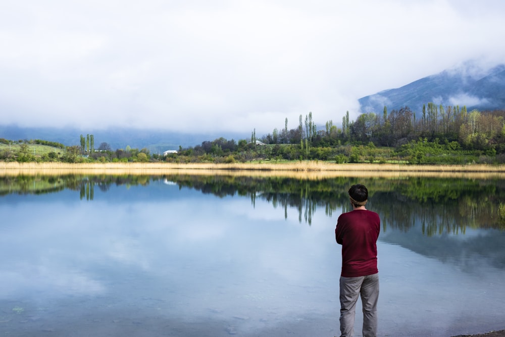 man standing near body of water and trees