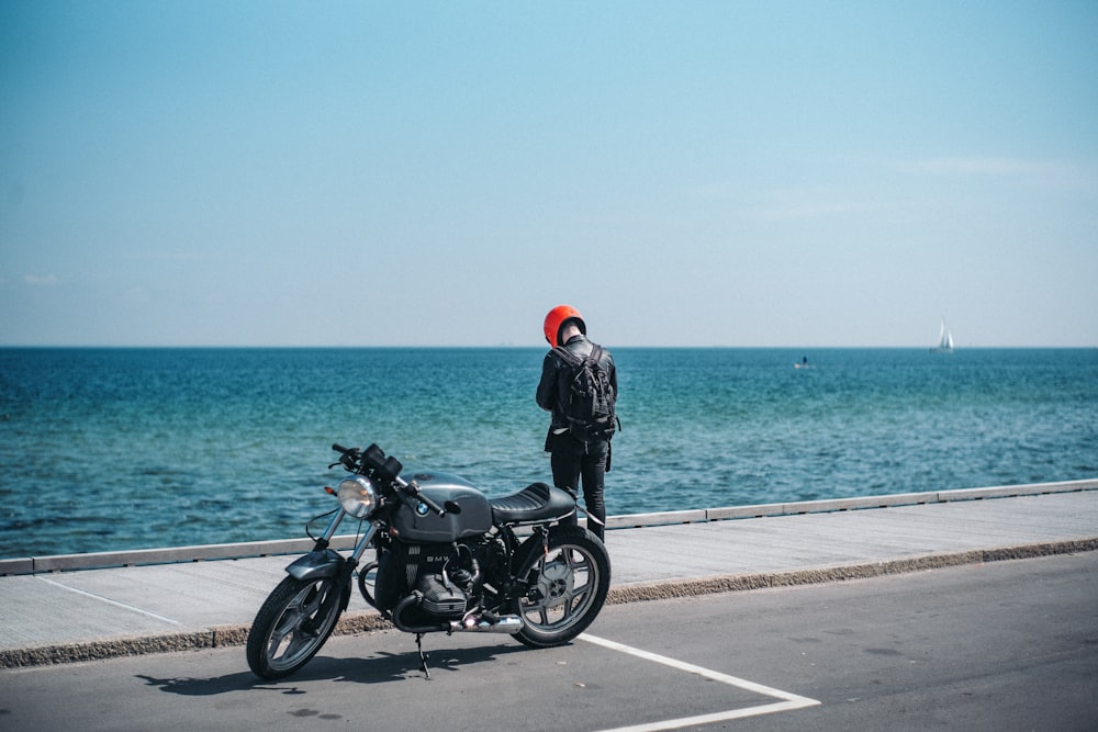 pessoa em pé ao lado da motocicleta perto do corpo d'água