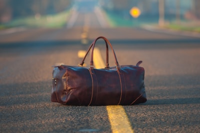 brown leather duffel bag in middle on gray asphalt road