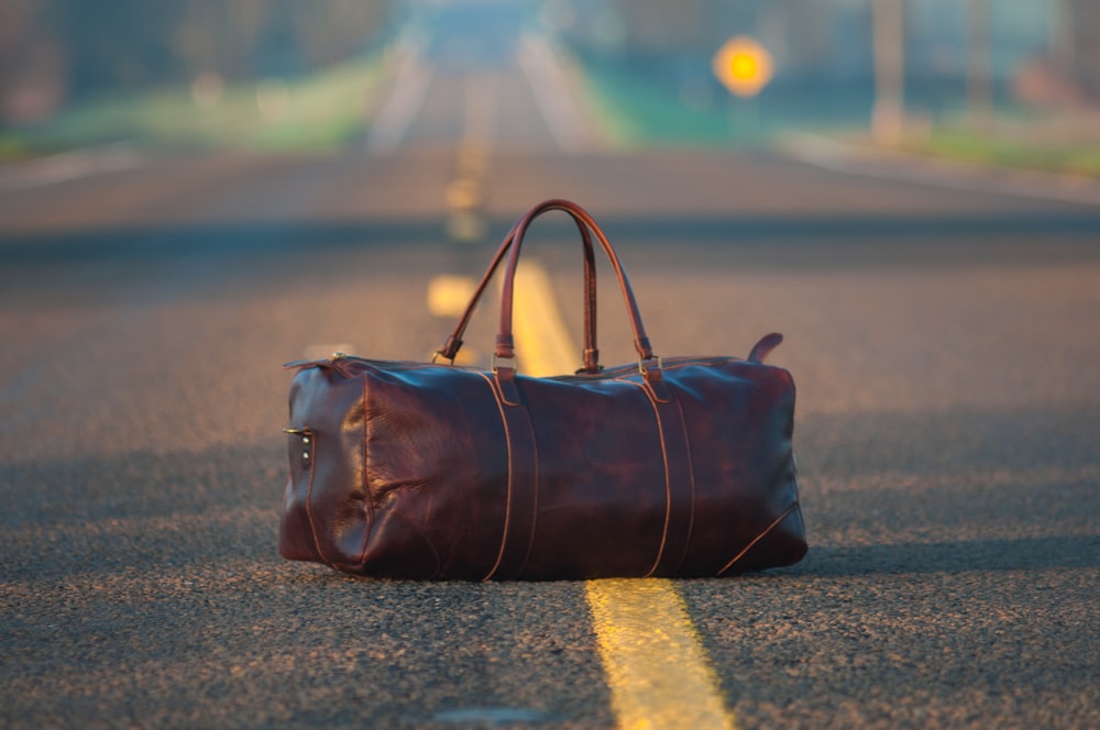 Sac de sport en cuir marron au milieu sur route asphaltée grise