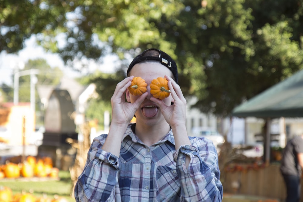 persona que viste una camisa de vestir azul abotonada sosteniendo dos calabazas naranjas