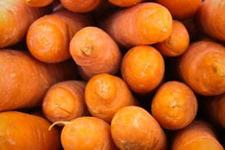Close-up of vibrant orange carrot powder in a clear glass bowl on a rustic wooden surface.