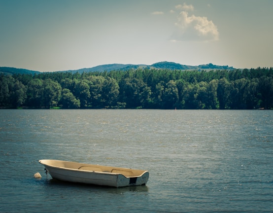 A small boat without a license gliding quietly on a serene lake surrounded by green hills.