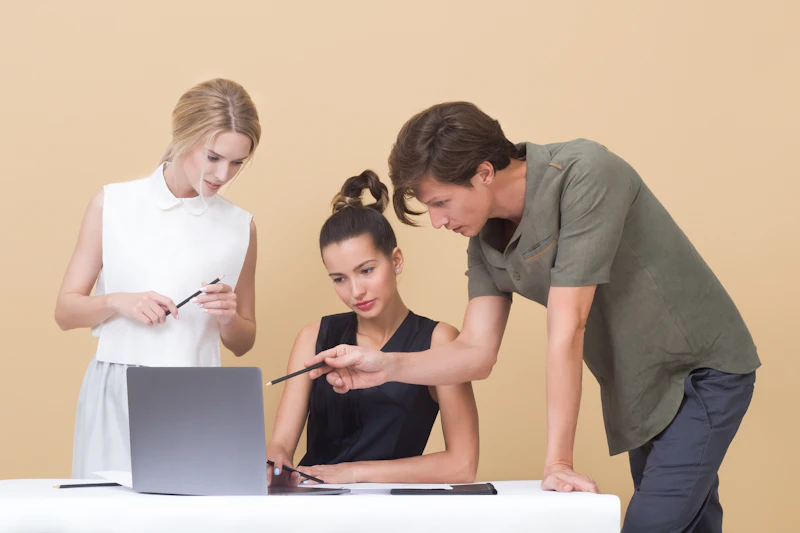 One person pointing at a laptop screen, explaining a step to another