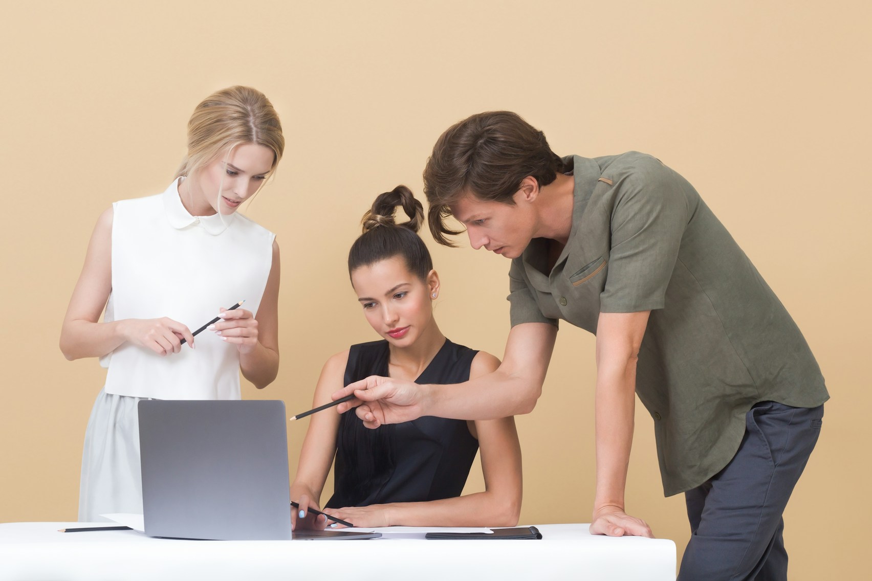 Three people collaborating at a white desk with a laptop
