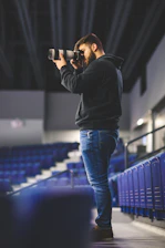 Candid black-and-white photo of a football creator capturing content with a DSLR in a vibrant stadium.