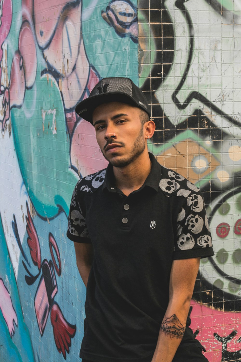 man wearing black and gray skull print polo shirt standing against the wall