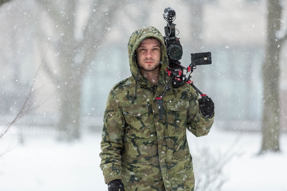 man in green and black camouflage hooded jacket holding black professional camera