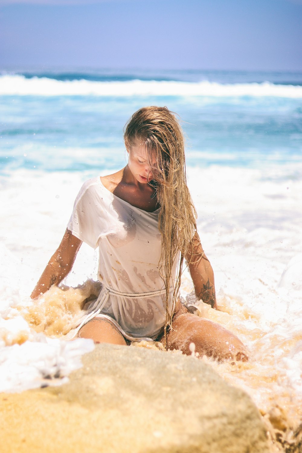 Mulher no topo branco sentado na areia perto do corpo da água