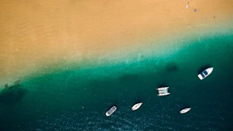 A panoramic view of crystal-clear waters with boats anchored near a sandy beach.