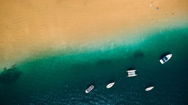 A panoramic view of crystal-clear waters with boats anchored near a sandy beach.