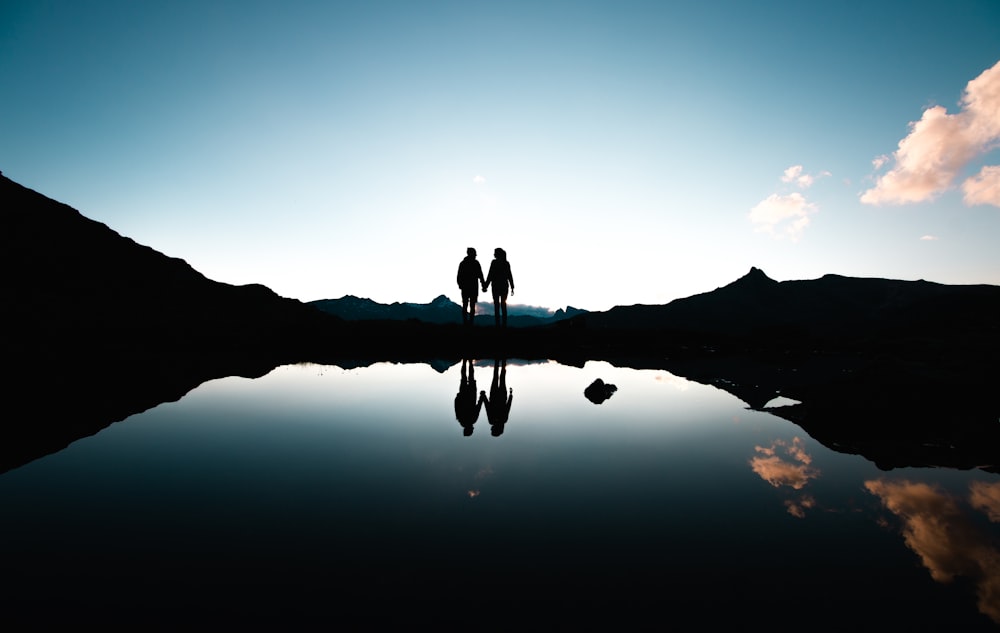 silhouette of people holding hands in front of body of water under blue sky