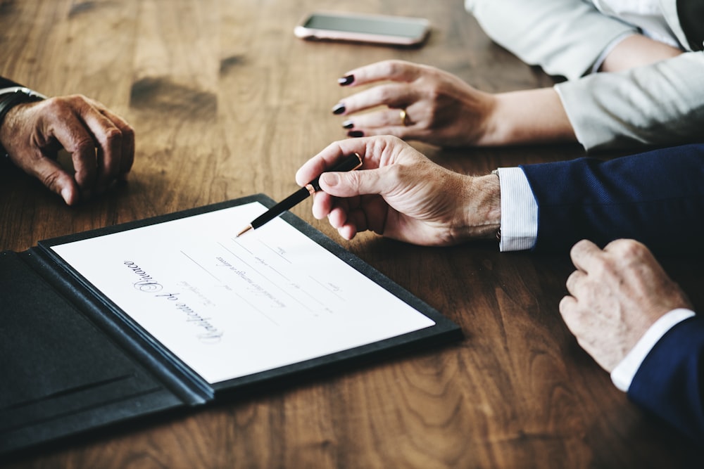 person holding black click pen signing on white paper