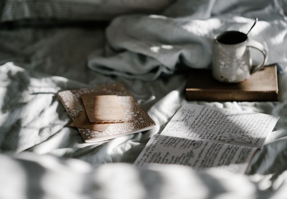 white mug on the bed beside journal