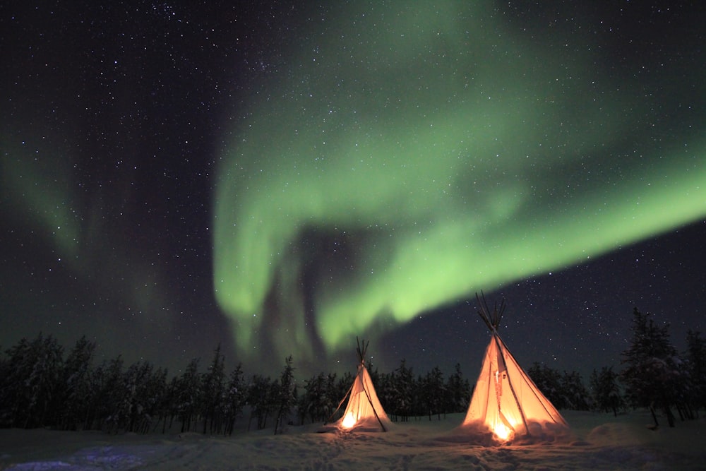 Tienda tipi iluminada bajo la aurora boreal verde