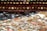 A large collection of assorted coins scattered across a surface, featuring different sizes and metallic shades. The coins have a weathered appearance, some reflecting light, and others appearing dull. In the background, there is an out-of-focus row of round objects resembling the coins, enhancing the depth of the image.