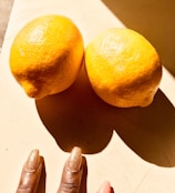 A hand with glossy, neon-colored press-on nails holding a sunlit lemon slice.