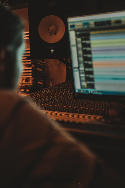 A dimly lit studio with gold accents, showing a focused artist and producer working together over a mixing console.