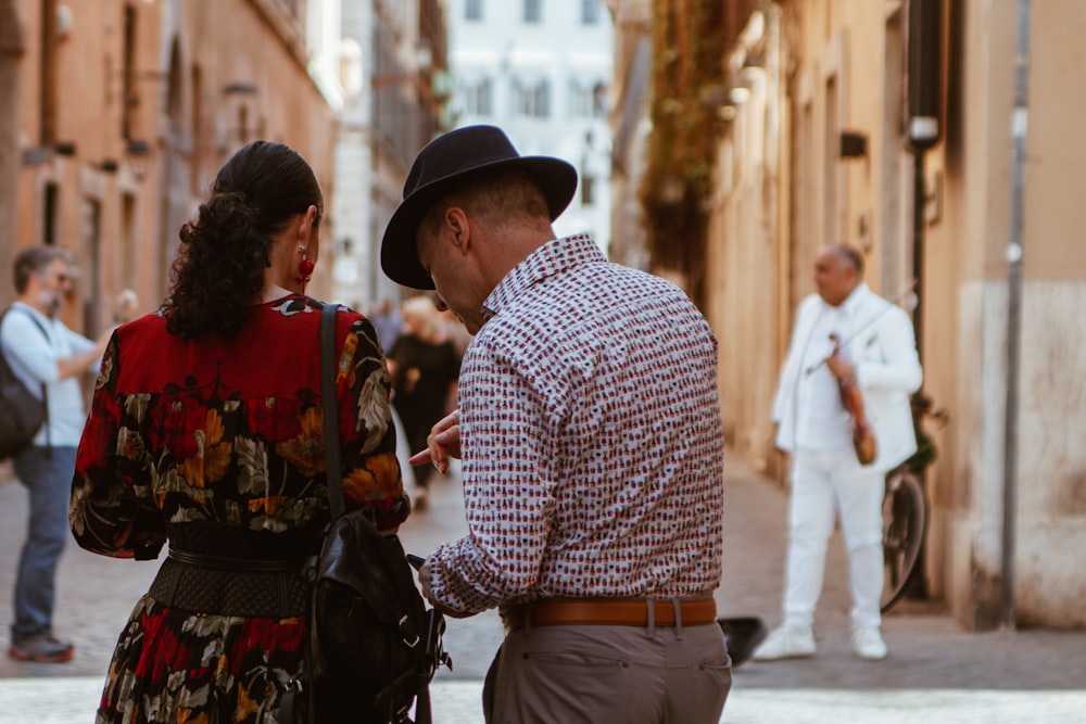 man in white and gray dress shirt beside woman in red, orange, and gray floral dress standing outside house