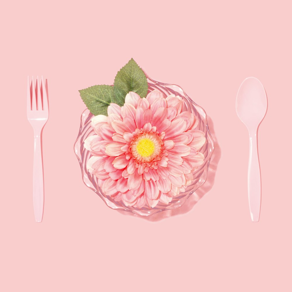 Photographie à plat de cuillère jetable, fourchette et fleur à pétales roses
