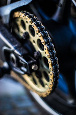 macro photography,how to photograph motorcycle chain and sprocket; selective focus photography of gold sprocket