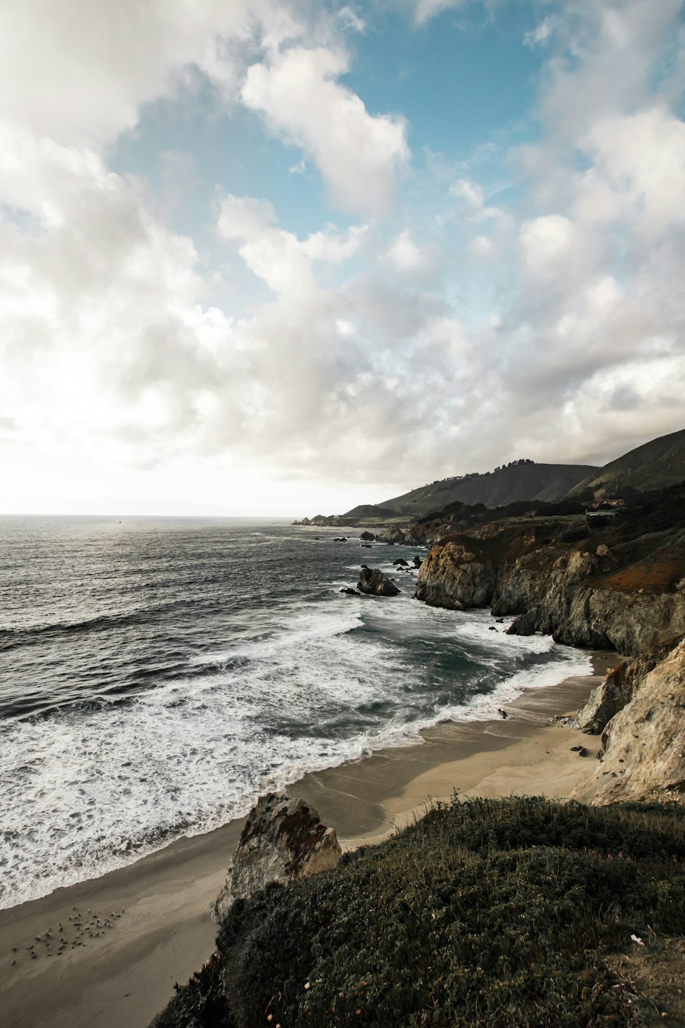 beach cliff viewing calm sea under white cloudy skies