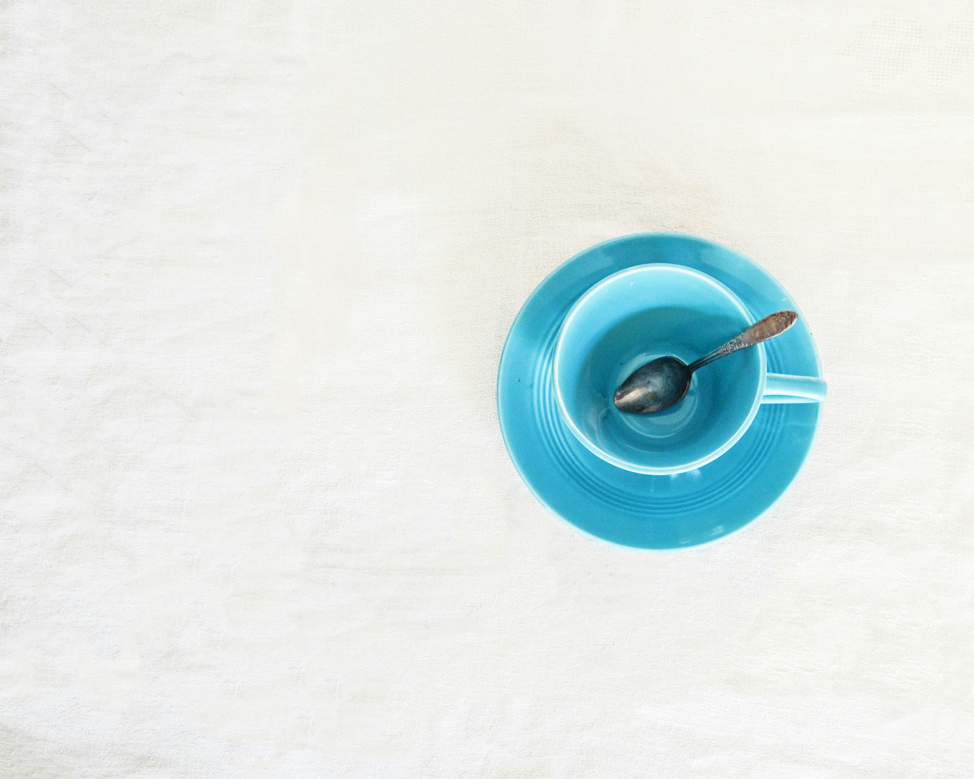 Small, empty blue cup with small spoon and saucer on a white-grey surface