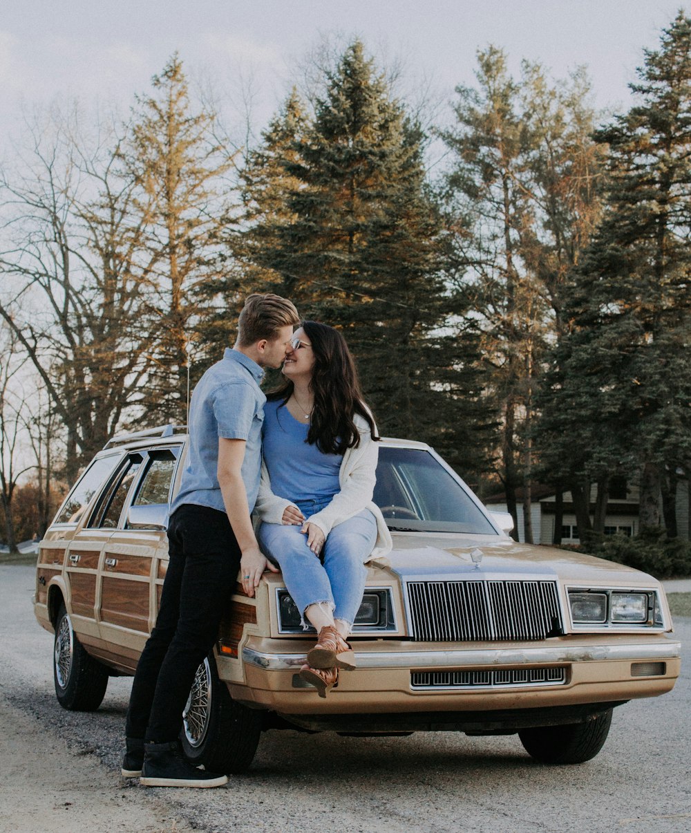 man kissing woman while sitting on brown car