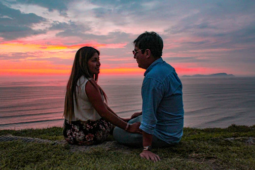 A couple enjoying a sunset dinner by the ocean with lanterns and gentle waves nearby.