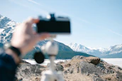 A close-up of a travel influencer capturing a scenic mountain landscape with a camera.