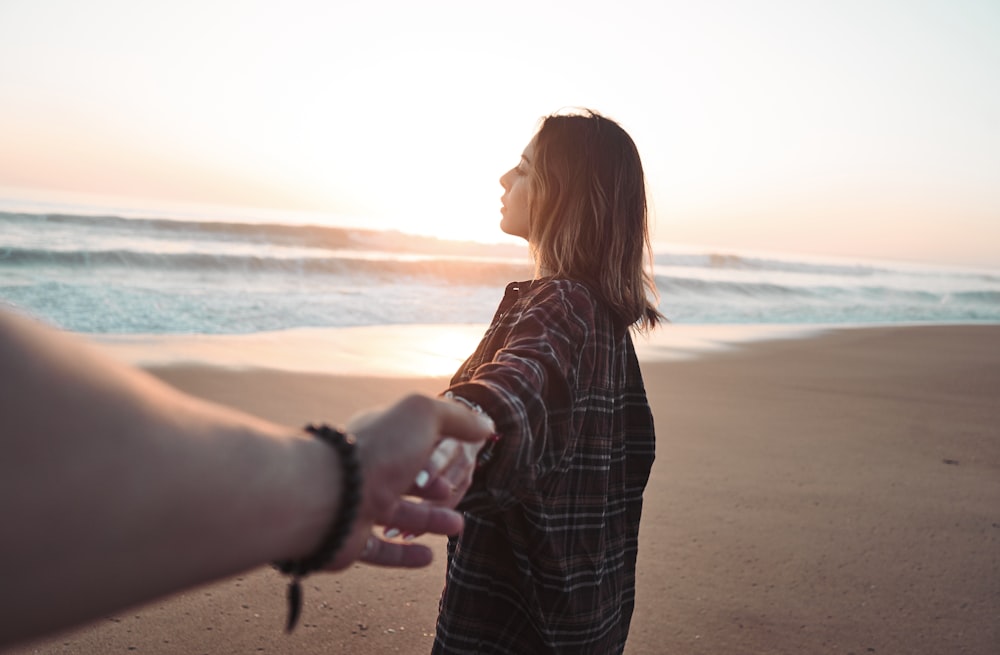 mulher de mãos dadas com a pessoa de frente para o oceano