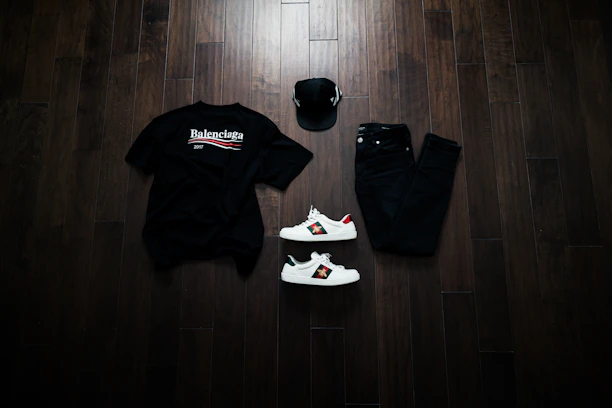 A sleek black and orange-themed flat lay of tracksuits, trousers, and t-shirts arranged on a dark surface.