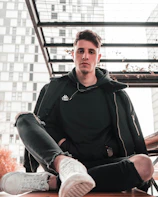 A man relaxing on a bench wearing a stylish hoodie and joggers, with a cityscape background.