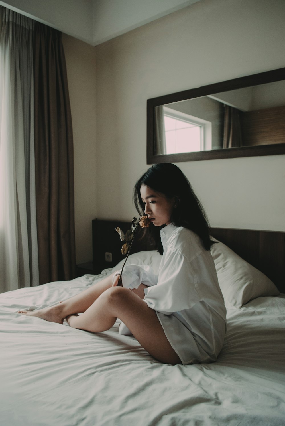 femme assise sur un lit blanc tenant une fleur