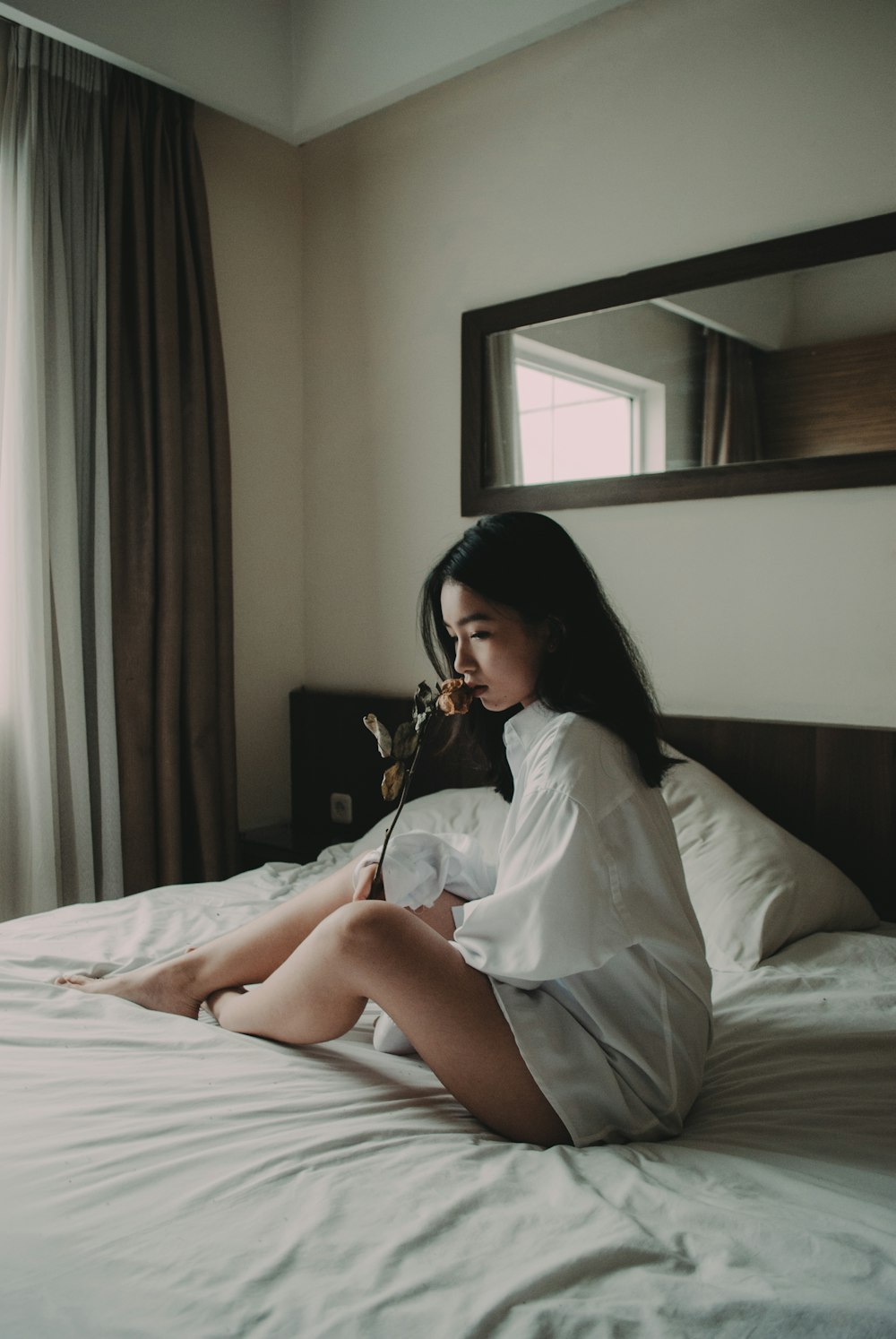 Mujer sentada en la cama blanca sosteniendo la flor