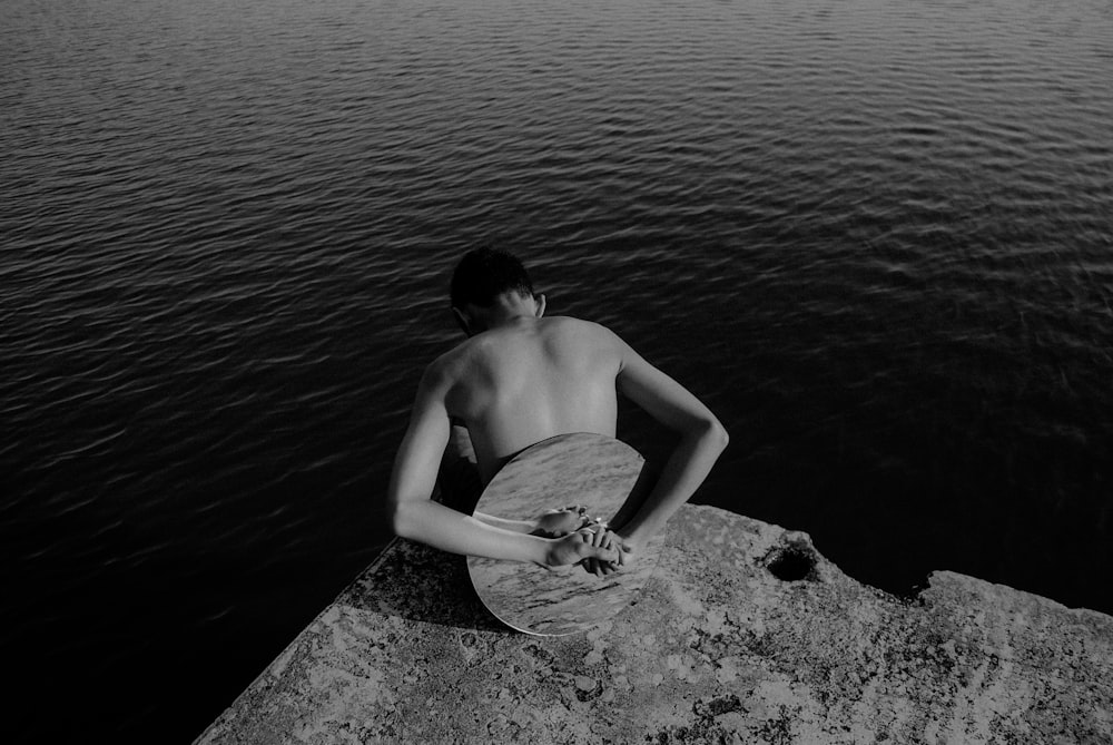 man with round mirror on his back at the edge of rock island facing body of water