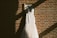 A beautifully styled wedding dress hanging on a sunlight-drenched window.
